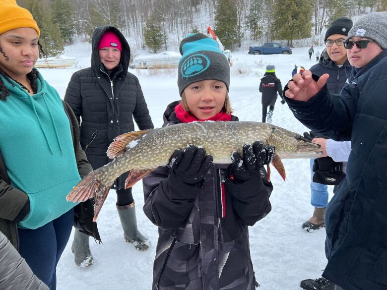 An Indigenous youth holds up a green and grey fish they caught while ice fishing 