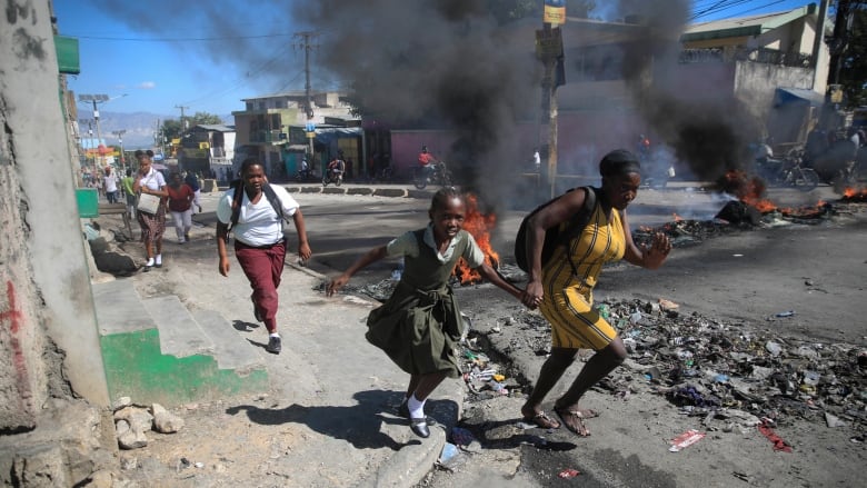  A woman and her daughter run past a barricade that was set up by police during a protest to denounce bad police governance in Port-au-Prince, Haiti.