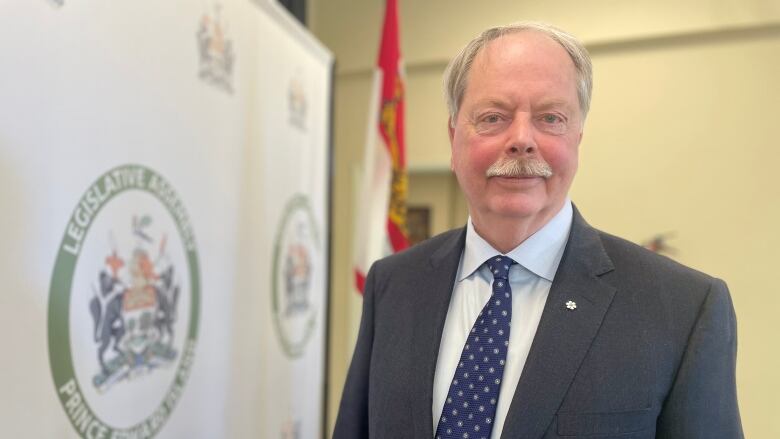 Man in a suit stands in front of PEI legislative assembly backdrop