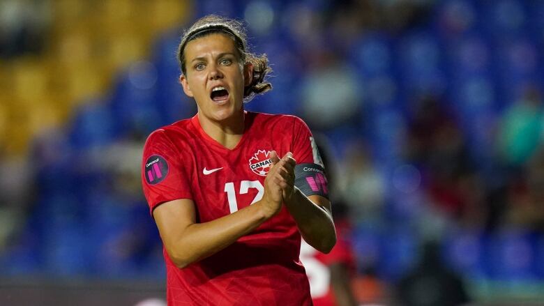 A women's player, in a red jersey, claps during a game.