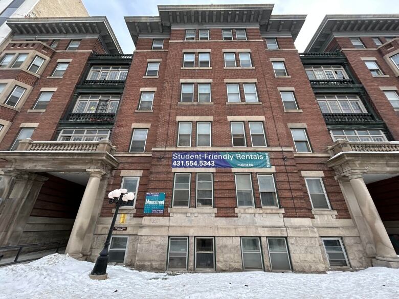 A five-storey brick apartment building is shown with signage reading student-friendly rentals and snow covering the sidewalk in front of the building.