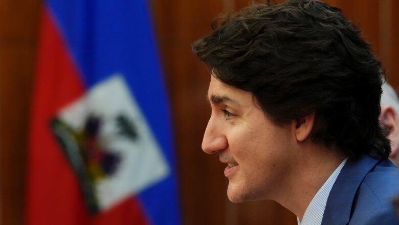 Prime Minister Trudeau sits in front of a Haitian flag.