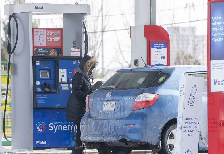 A woman fills up a car with gasoline in winter.