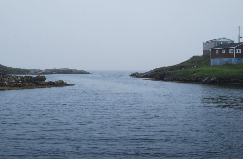 An oceanside scene of small islands and calm waters, with houses on an island on the right.