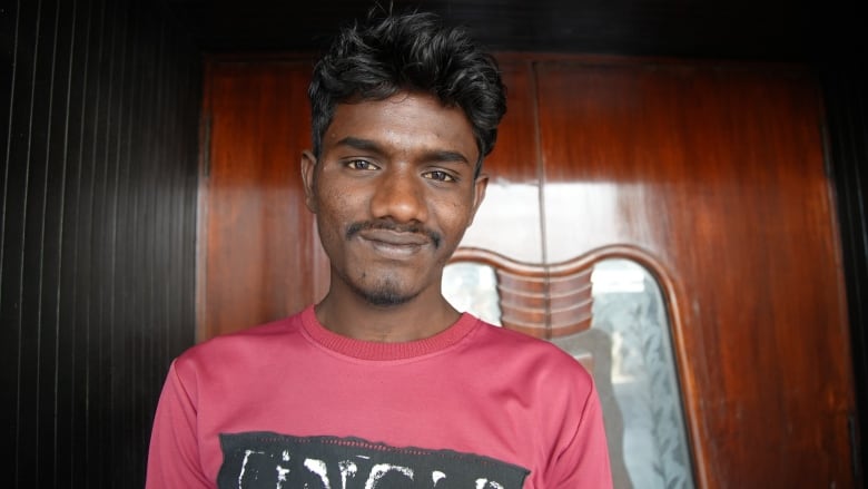 A man wearing a red T-shirt with a black design on the front poses for a portrait outside the dark wooden doors of an old movie theatre.