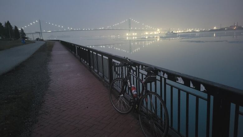 A bike stands up against a railing on the misty Detroit River in the dark.