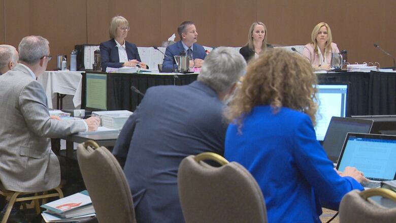 A panel of people in the background and a row of individuals on laptops in the foreground