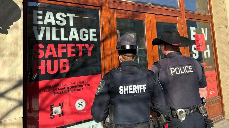 A Sheriff and a police officer look into a window at the East Village Safety Hub.