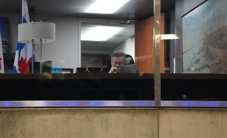 A man reads from a sheet of paper through the window of an office.