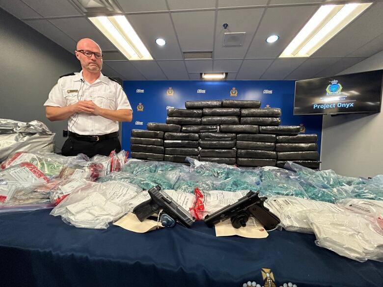 A police officer looks over a table covered with bags and bricks of drugs, guns and other items.