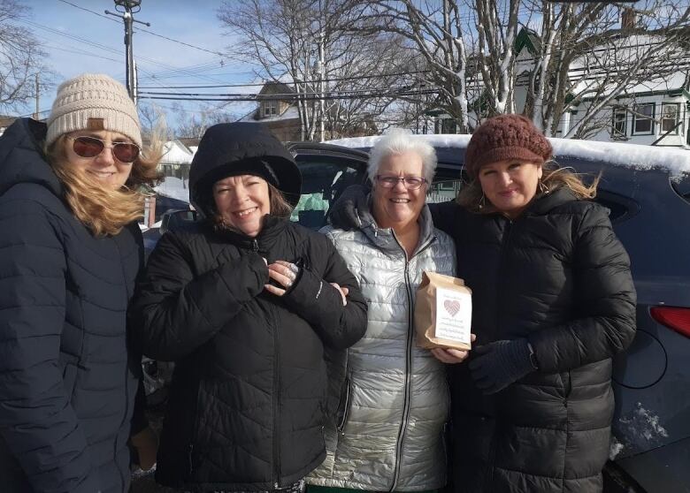 Four women wearing parkas stand outside in front of an SUV.