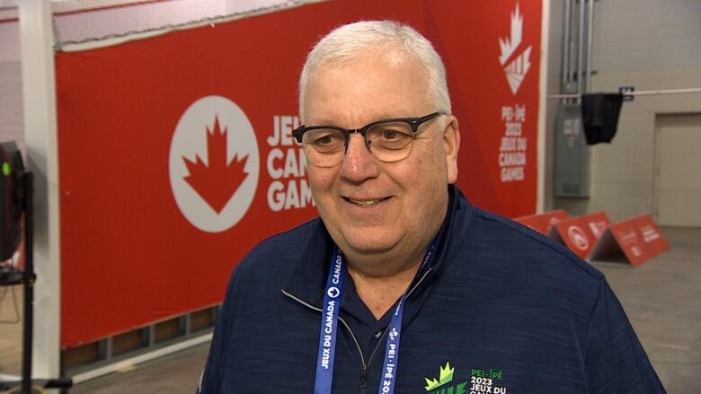 man stands in front of Canada Games backdrop, wearing Canada Games shirt and lanyard