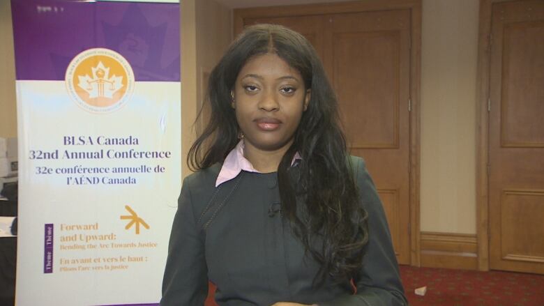 A woman wearing a grey blazer stands next to a sign that says 