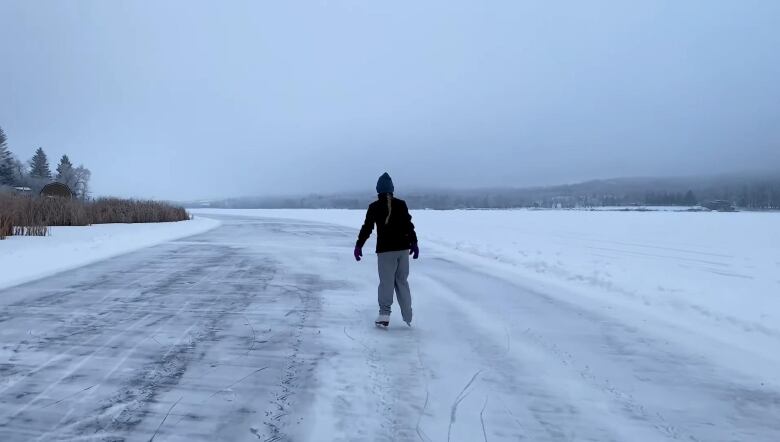 A girl is seen skating on a trail on a frozen pond.