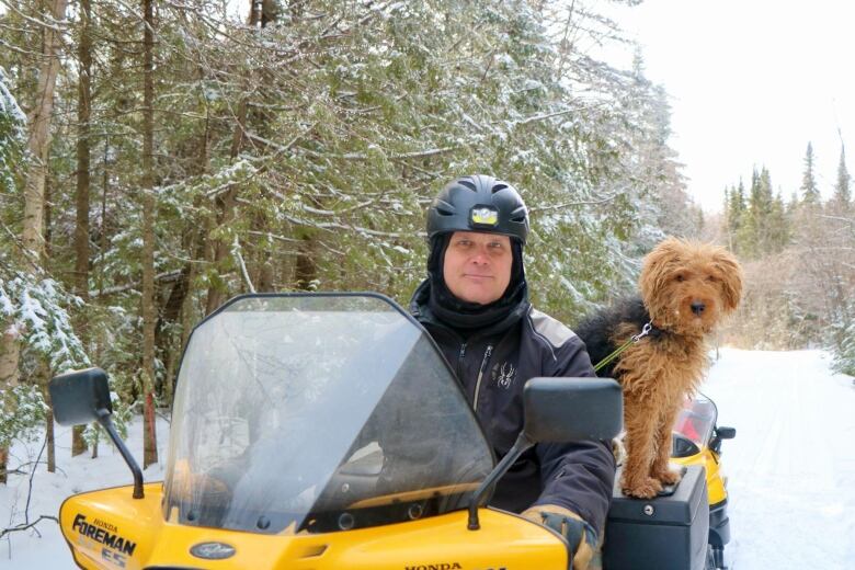 A man in a ATV in the snow. His dog is in the ATV.