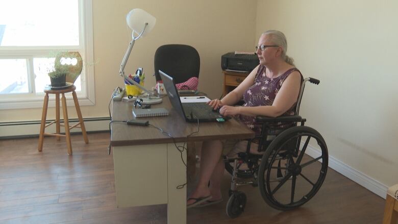 A wide shot of a woman using a wheelchair sitting at a desk.