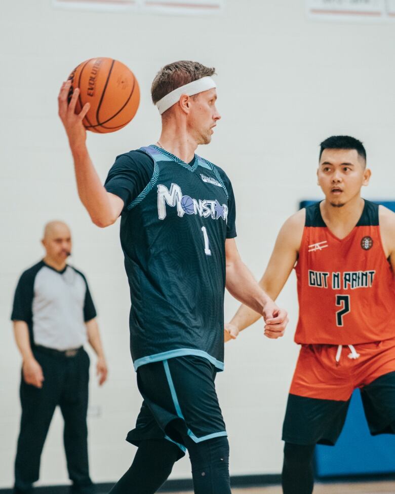 A man holding a basketball in his right hand is being challenged by a defender in a basketball game.