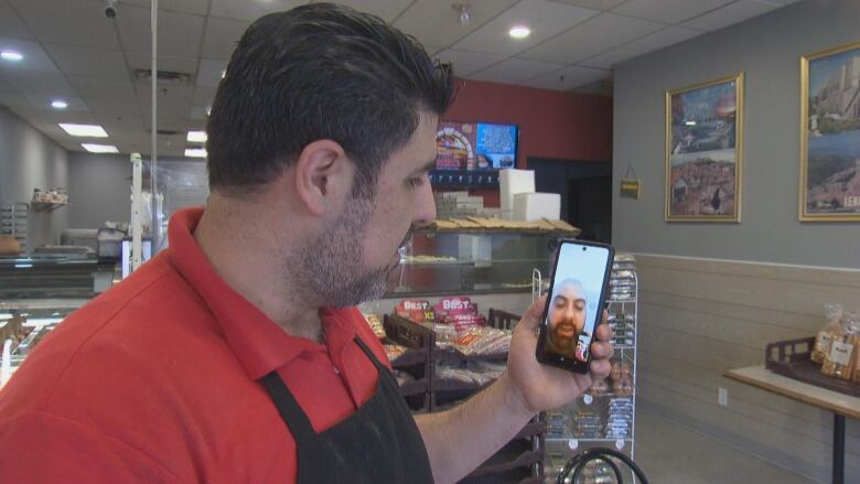 A man in a bakery holding a phone and talking on a video call. 