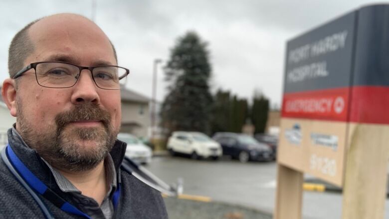 A man takes a selfie in front of a hospital sign