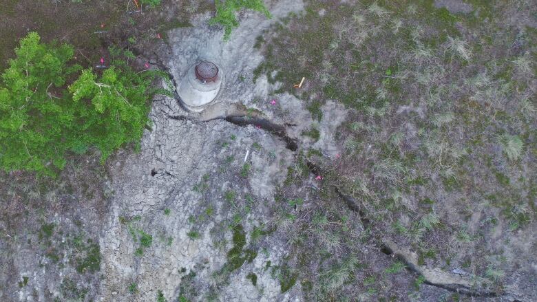 An overhead view of a manhole on a treed slope, with a large crack in the soil.