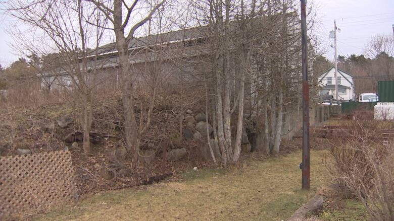 The back of a building is seen with trees and rocks on a sloped portion of the ground.