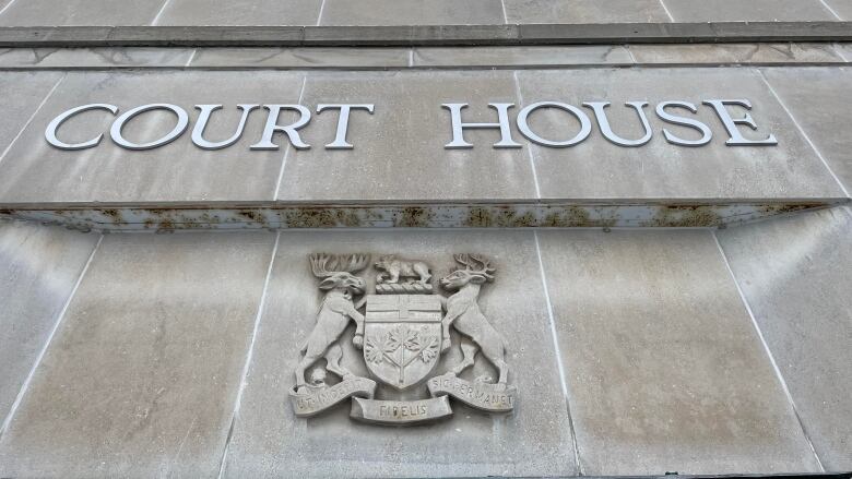 A grey stone block wall with the words 'Court House' and the coat of arms of Ontario.