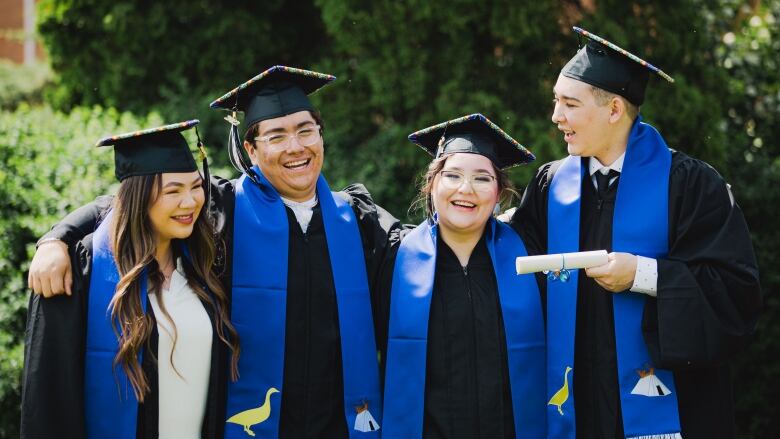 A group of Indigenous graduates stand in caps and gowns smiling and celebrating their success.