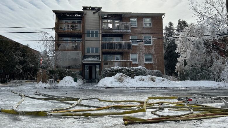 An apartment building with ice on the front and roof damage. There's a fire hose on the ground in front of it.