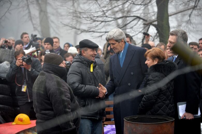 An elderly man shakes hands with another man at a memorial.