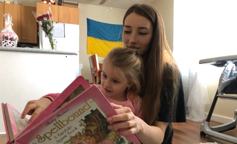 A woman and her daughter read a book.