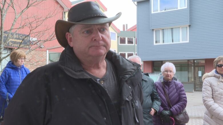 A man in a cowboy hat stands looking at a person next to the camera.