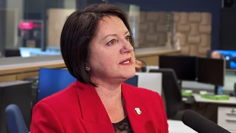 A portrait of a woman with short, dark hair speaking into a reporter's microphone.