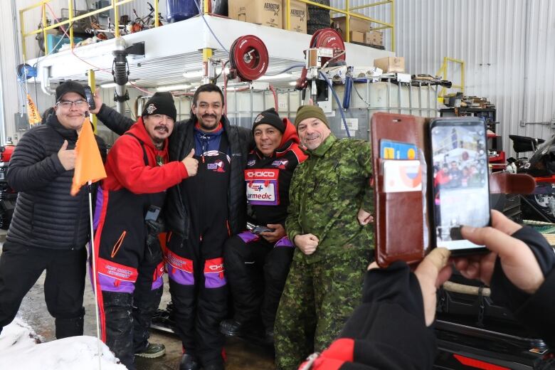 A group of Indigenous men stand with their arms around each other as an unidentified person takes a photo with their phone. 