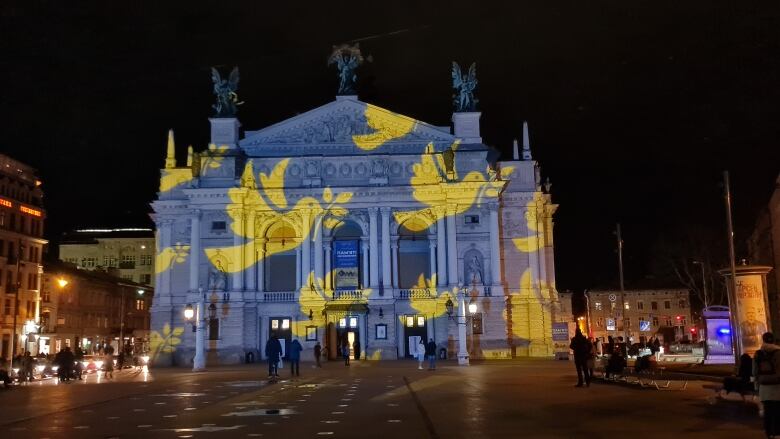 The outside face of an opera house in Ukraine is lit up by a projection. The image shows yellow doves flying on a blue background, matching the colours of the Ukrainian flag.