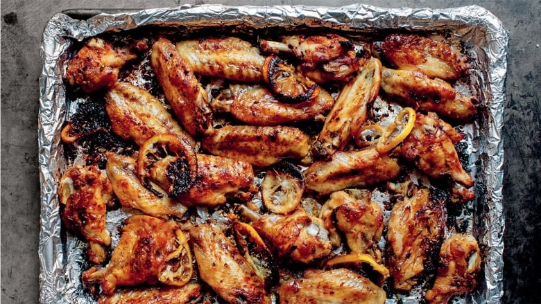 Roasted chicken wings and lemon slices on a baking sheet covered in tin foil, sitting on a grey surface.