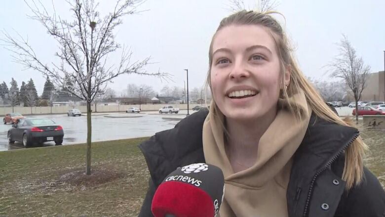 A close-up of Sadie Cartwright speaking into a CBC microphone, gray sky and wet lawn behind her.