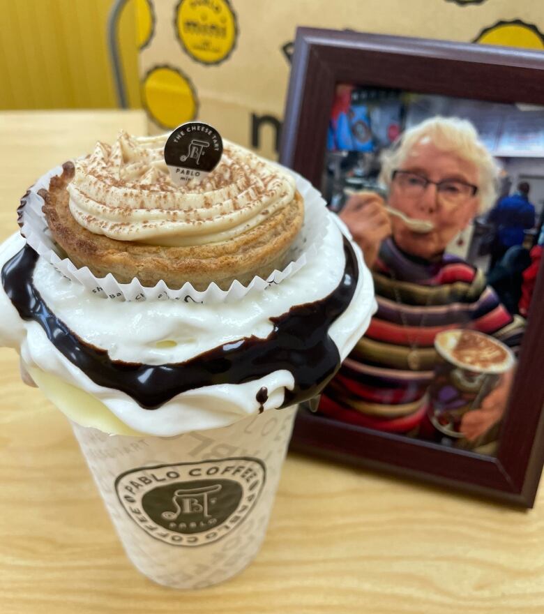 A photo of a woman enjoying a hot chocolate sits behind another extravagent cup of hot chocolate.