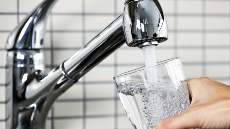 Water streaming out of a stainless steel faucet into a glass