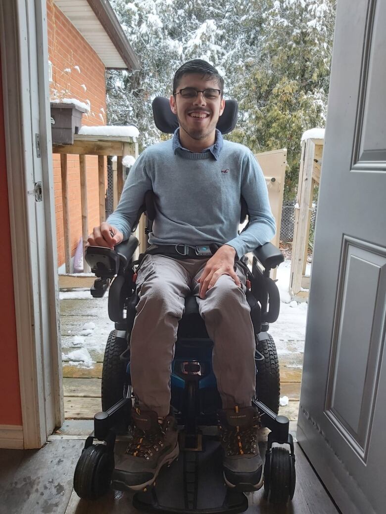 A man sits in a power chair in an doorway which opens to a snowy platform.