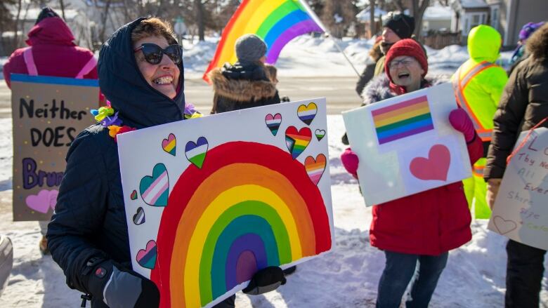 Ralliers dressed in winter gear hold pro LGBTQ signs.