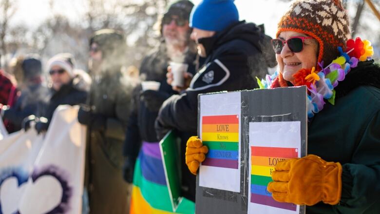 Ralliers dressed in winter gear hold pro LGBTQ signs.