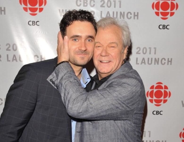 One man holds a second man's face as they look at the camera on a red carpet.