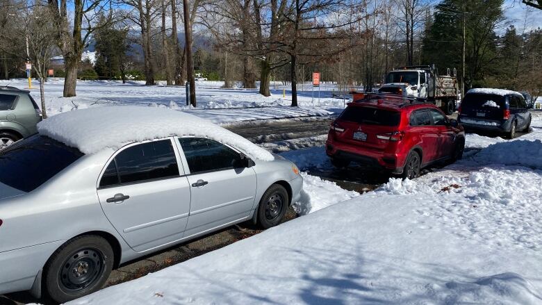 Snow covers the ground and parked cars on a street. 