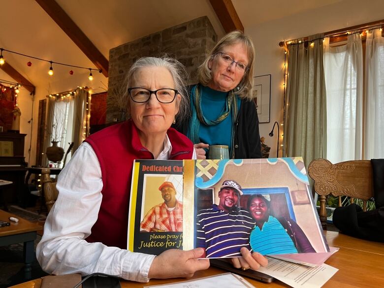 Two older women looking at the camera while holding two pictures.