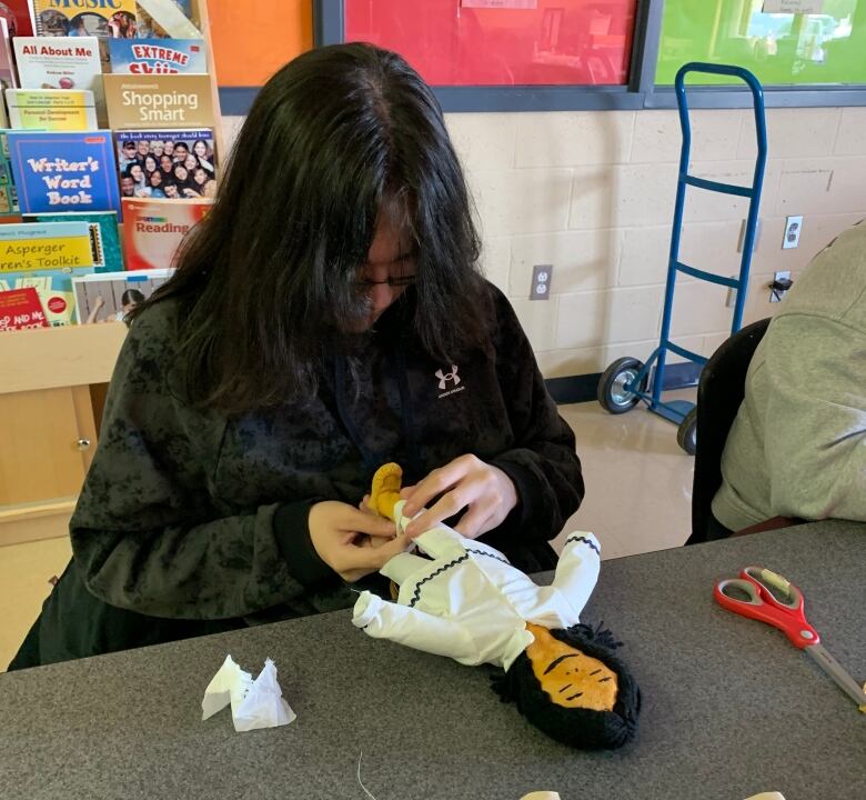 A teenager with black hair sews the legs of a traditional doll made. 