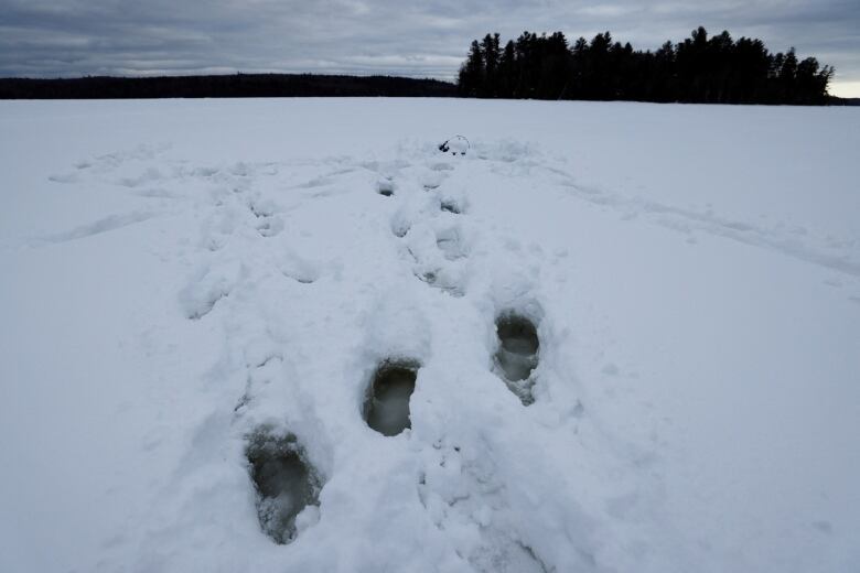 A line of boot prints on a lake with three that sank into a hidden pocket of slush.