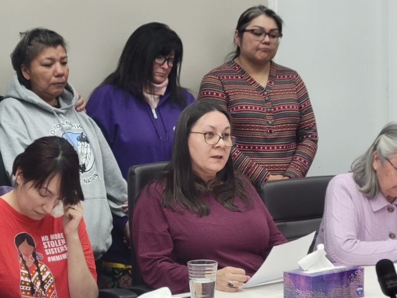 A woman in a purple shirt reads a statement on white paper into the microphone