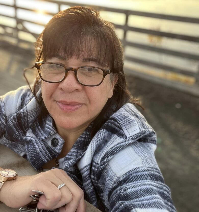 An Indigenous woman with glasses with a sun behind her 