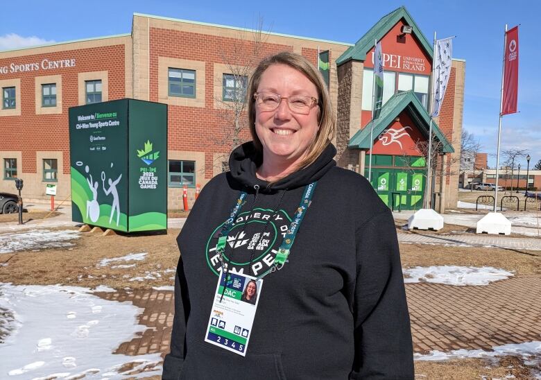 Woman in Team PEI hoodie and security pass stands in front of arena at UPEI. 