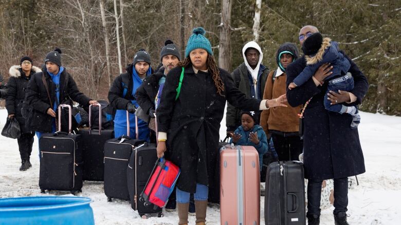 Migrants seen carrying suitcases in the snow.